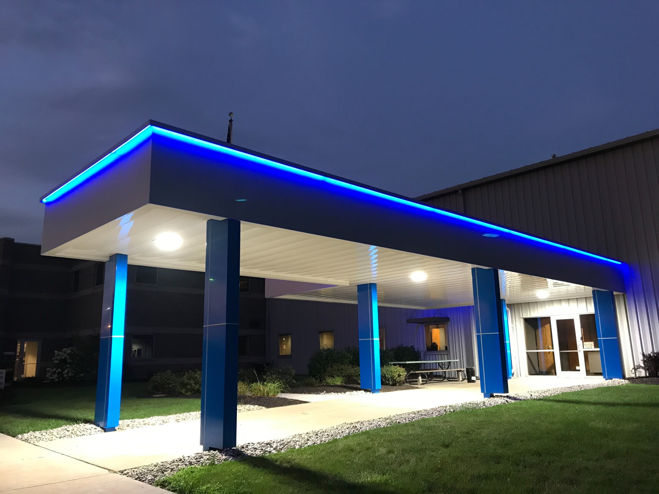 Architectural walkway canopy with bright blue eyebrow lighting.
